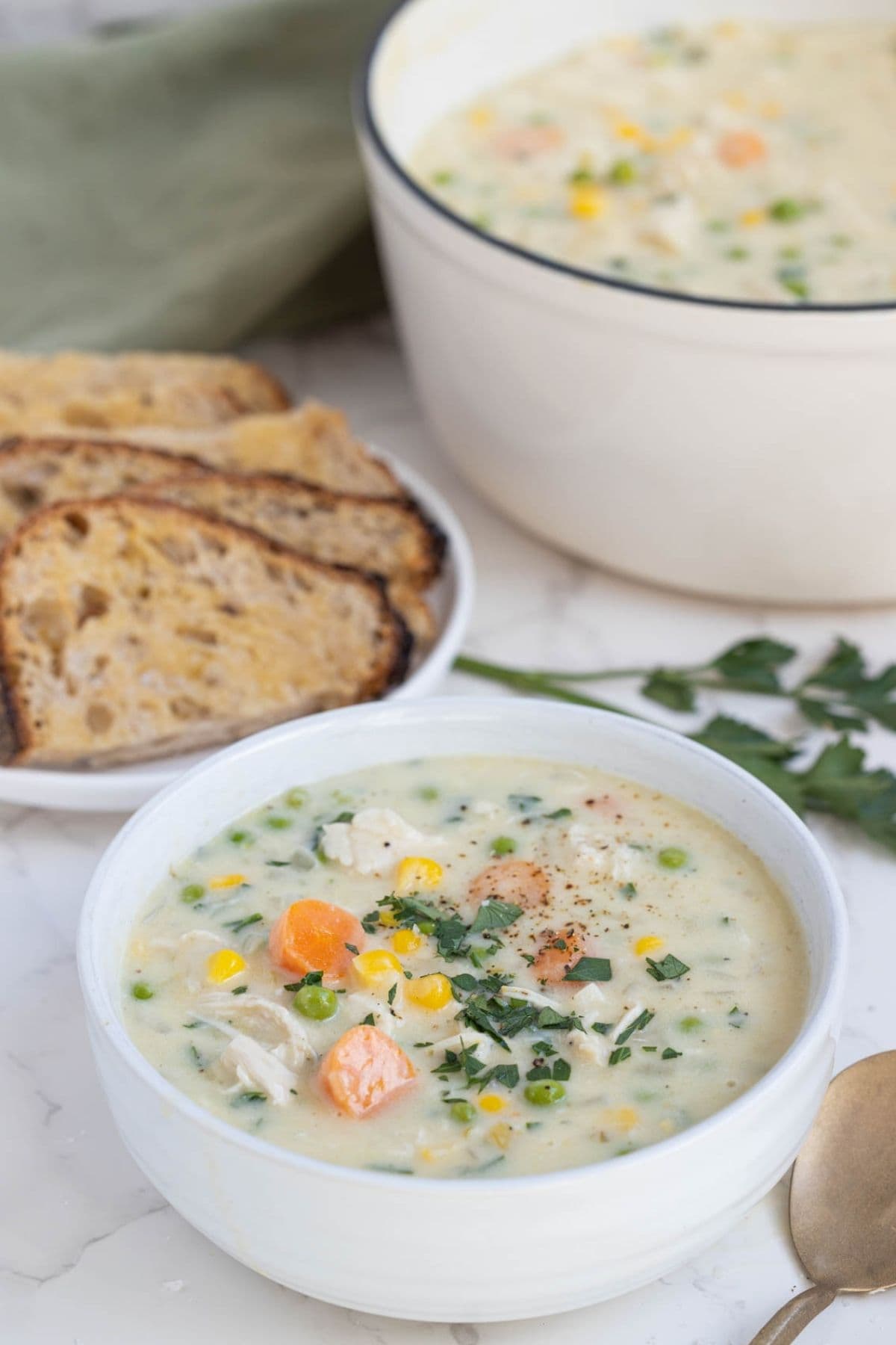 A bowl of sourdough chicken pot pie soup served with a plate of fresh sourdough bread.