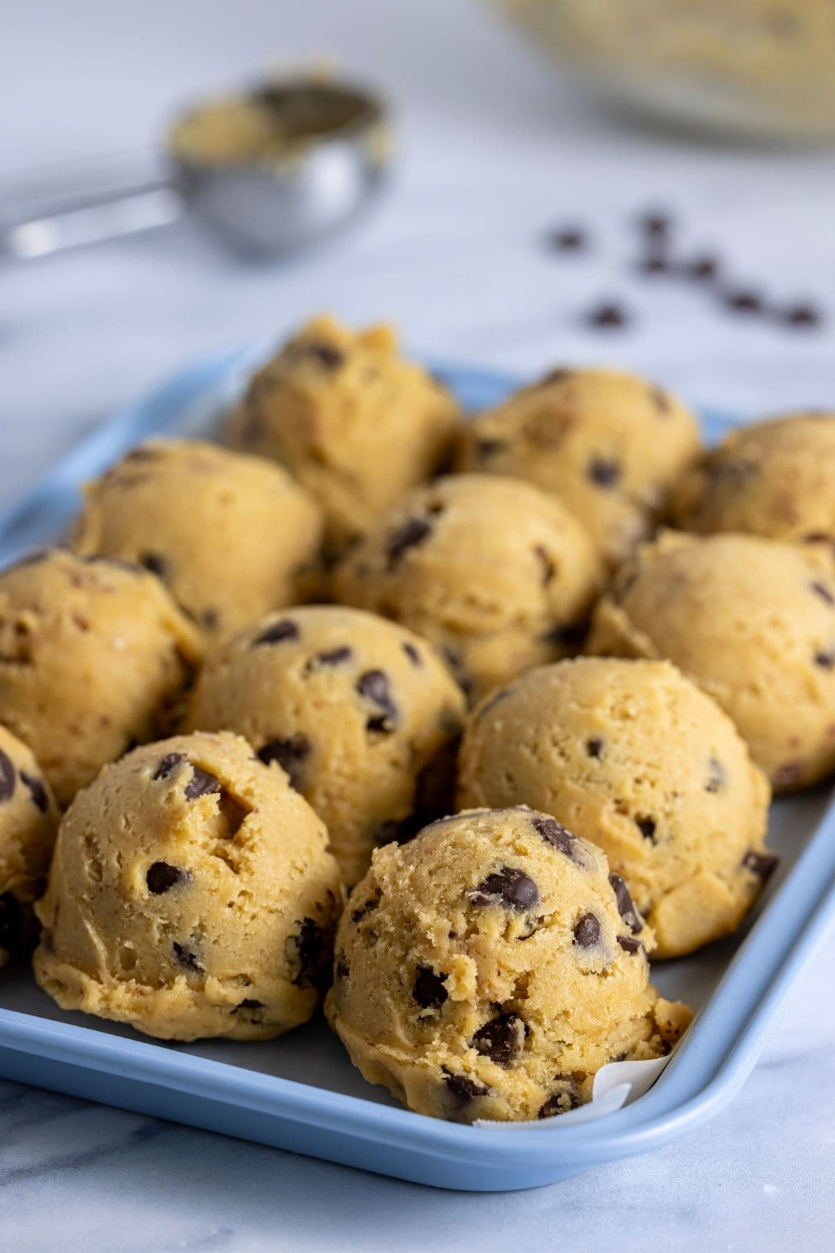 A pale blue baking try with 12 cookie dough balls ready to be frozen.