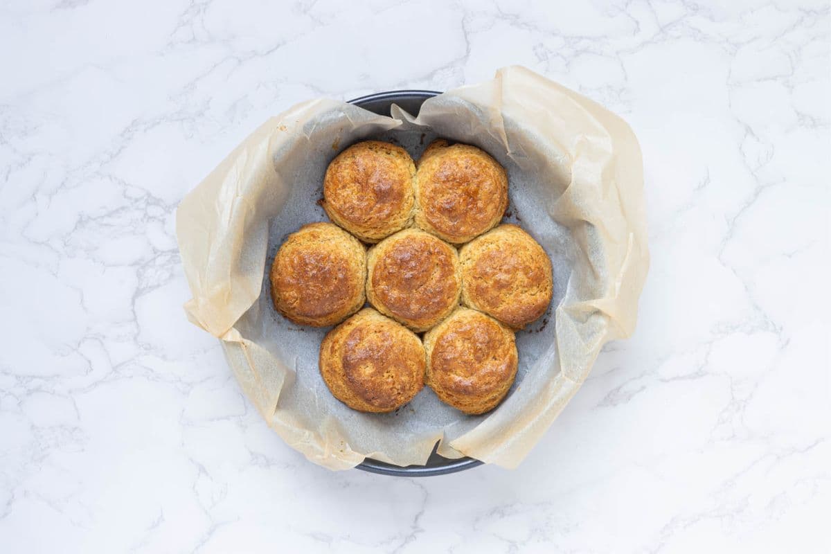 A round cake pan containing 7 sourdough cornbread biscuits that are fresh out of the oven and golden brown.