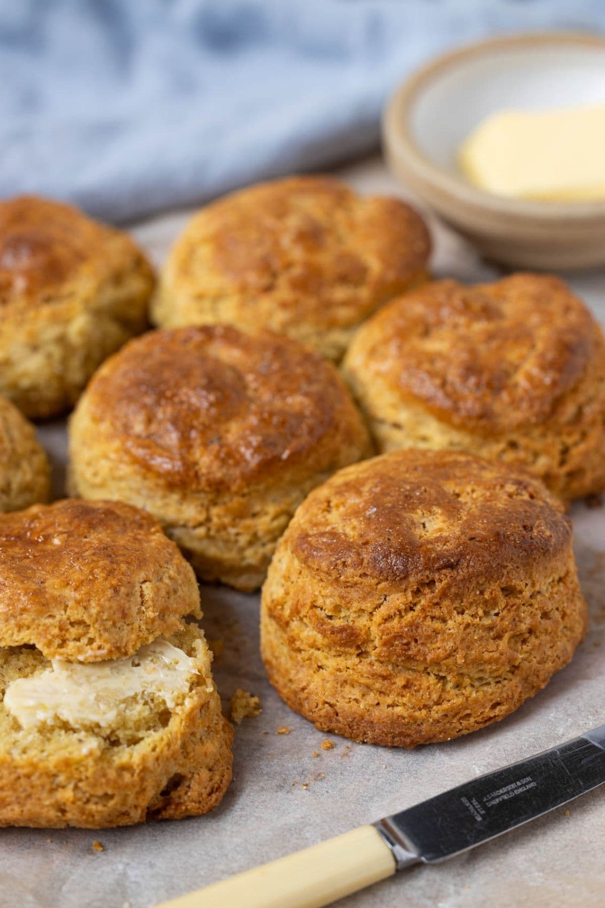 A batch of golden brown sourdough cornbread biscuits. You can see a small bowl of butter in the background of the image.
