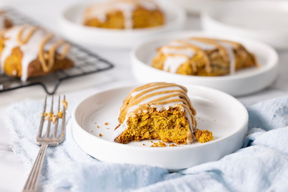 Horizontal image of a sourdough pumpkin scone that has the first part broken off so you can see the texture inside. There are other scones in the background.