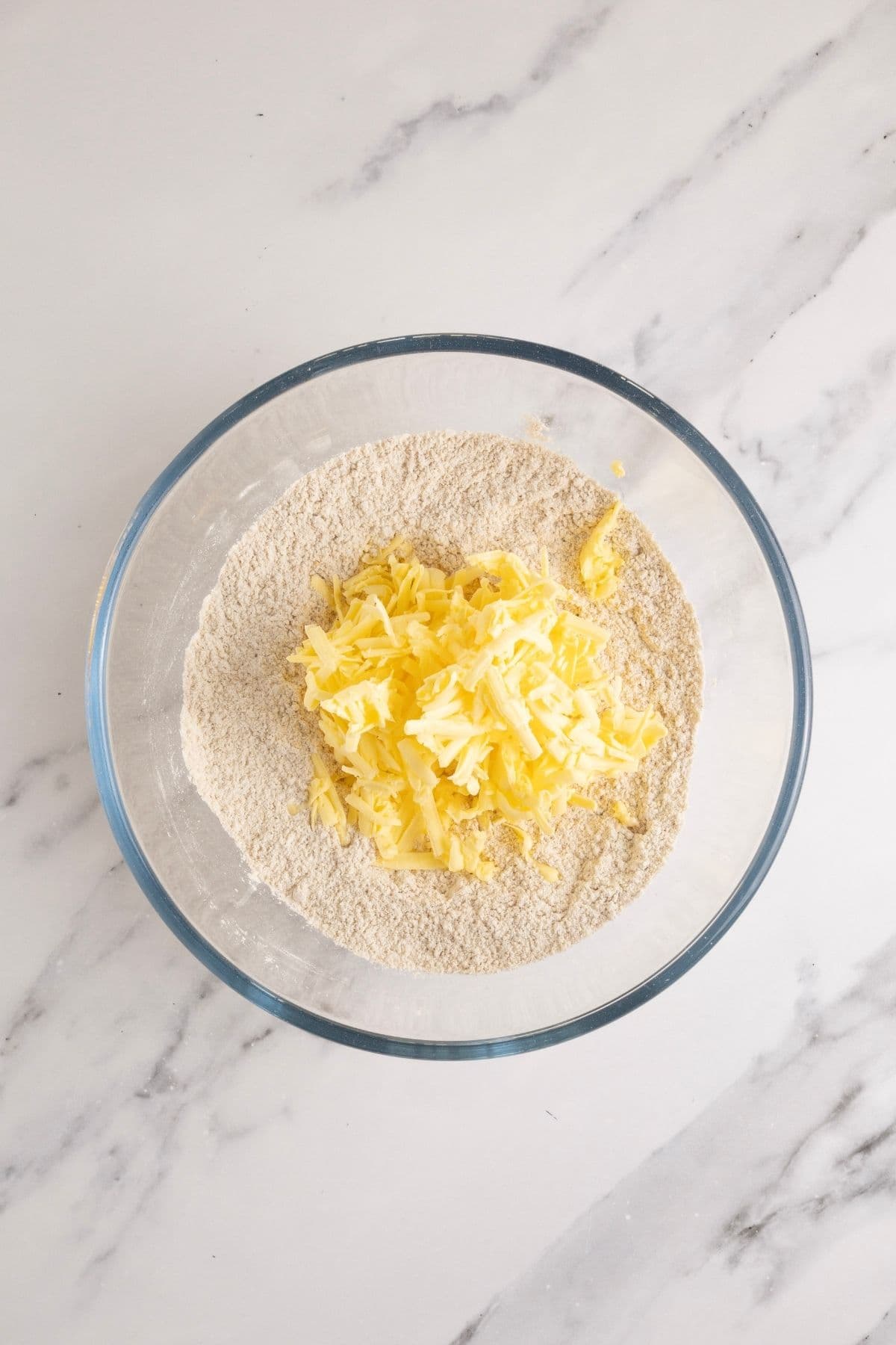A glass bowl filled with the dry ingredients and the cubed butter on top.