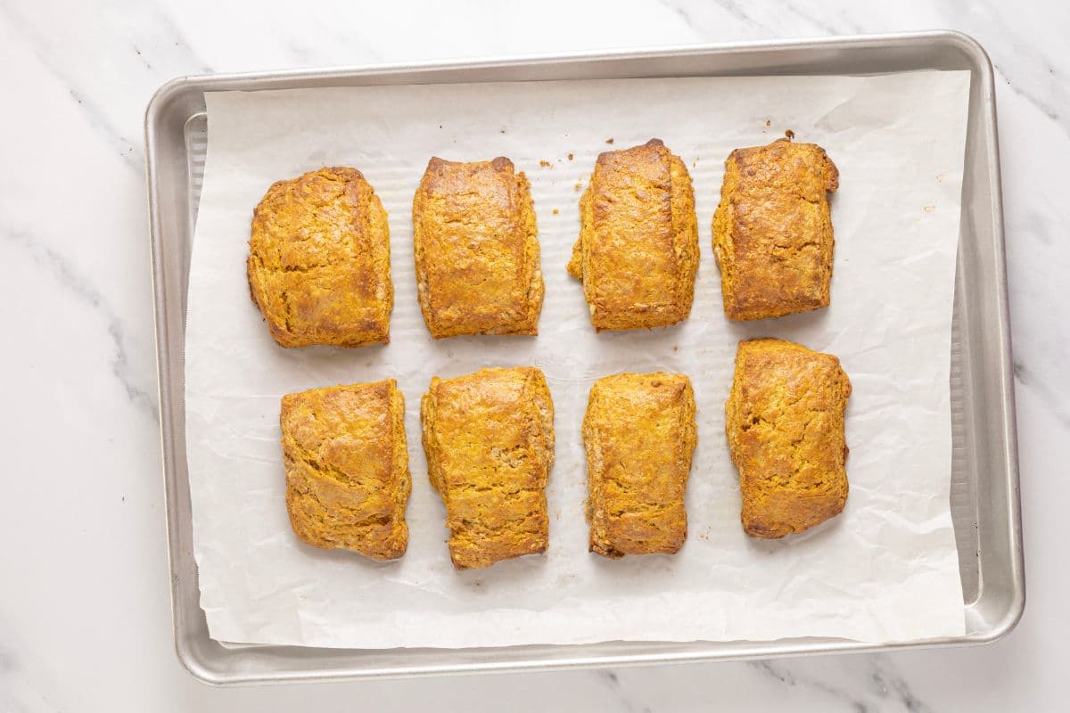 A baking tray holding 8 sourdough pumpkin scones that have just been taken out of the oven.