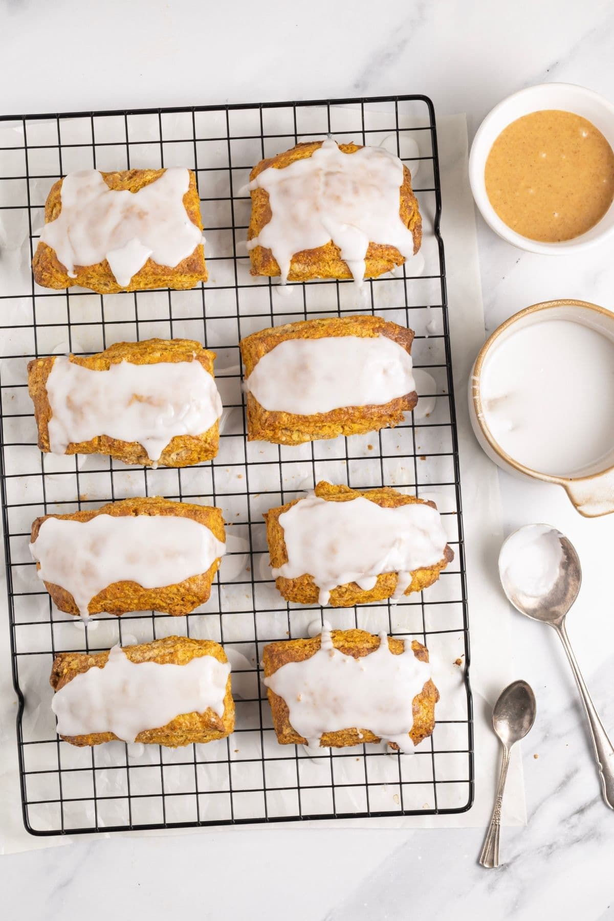 8 flaky sourdough pumpkin scones that are sitting on a wire cooling rack and have been drizzled with a white glaze.