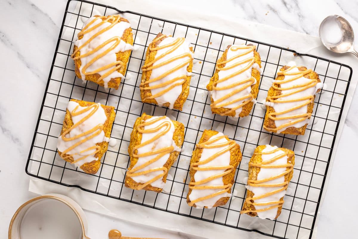 A horizontal image showing the finished sourdough pumpkin scones that have been drizzled with a white glaze and then piped with a pumpkin spice glaze.