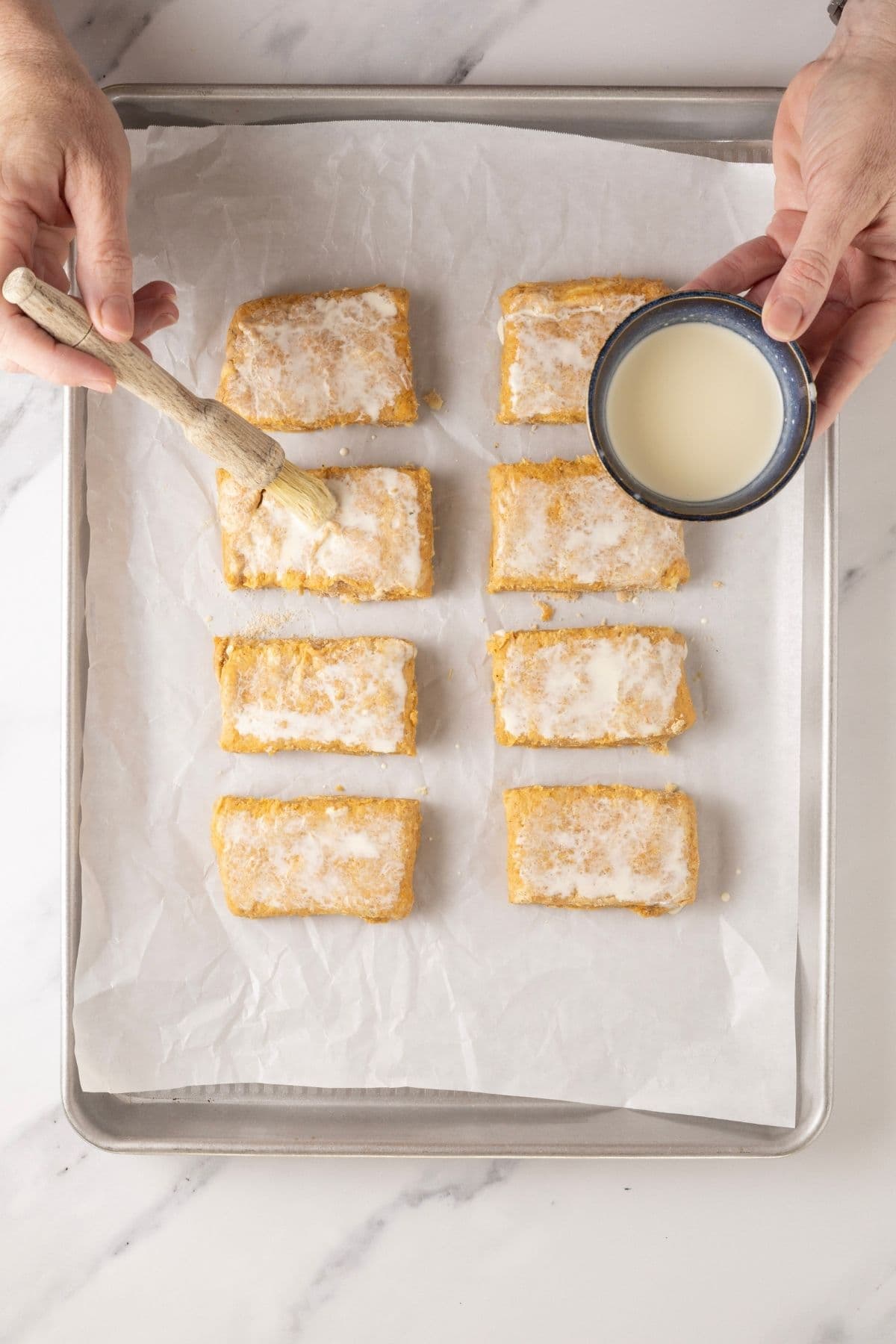 8 equal pieces of sourdough pumpkin scone dough being brushed with milk on a tray.