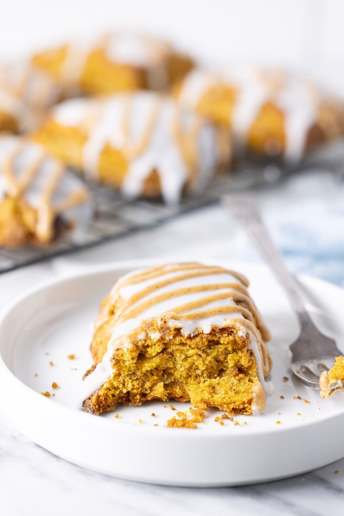 A close up vertical image with a sourdough pumpkin scone in the centre. You can see the flaky texture inside. There are more scones cooling on a wire rack in the background.
