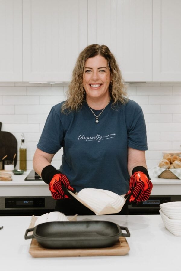 A photo of Kate Freebairn, founder of The Pantry Mama, placing a loaf of sourdough into a black cast-iron bread pan ready to place it into the oven.