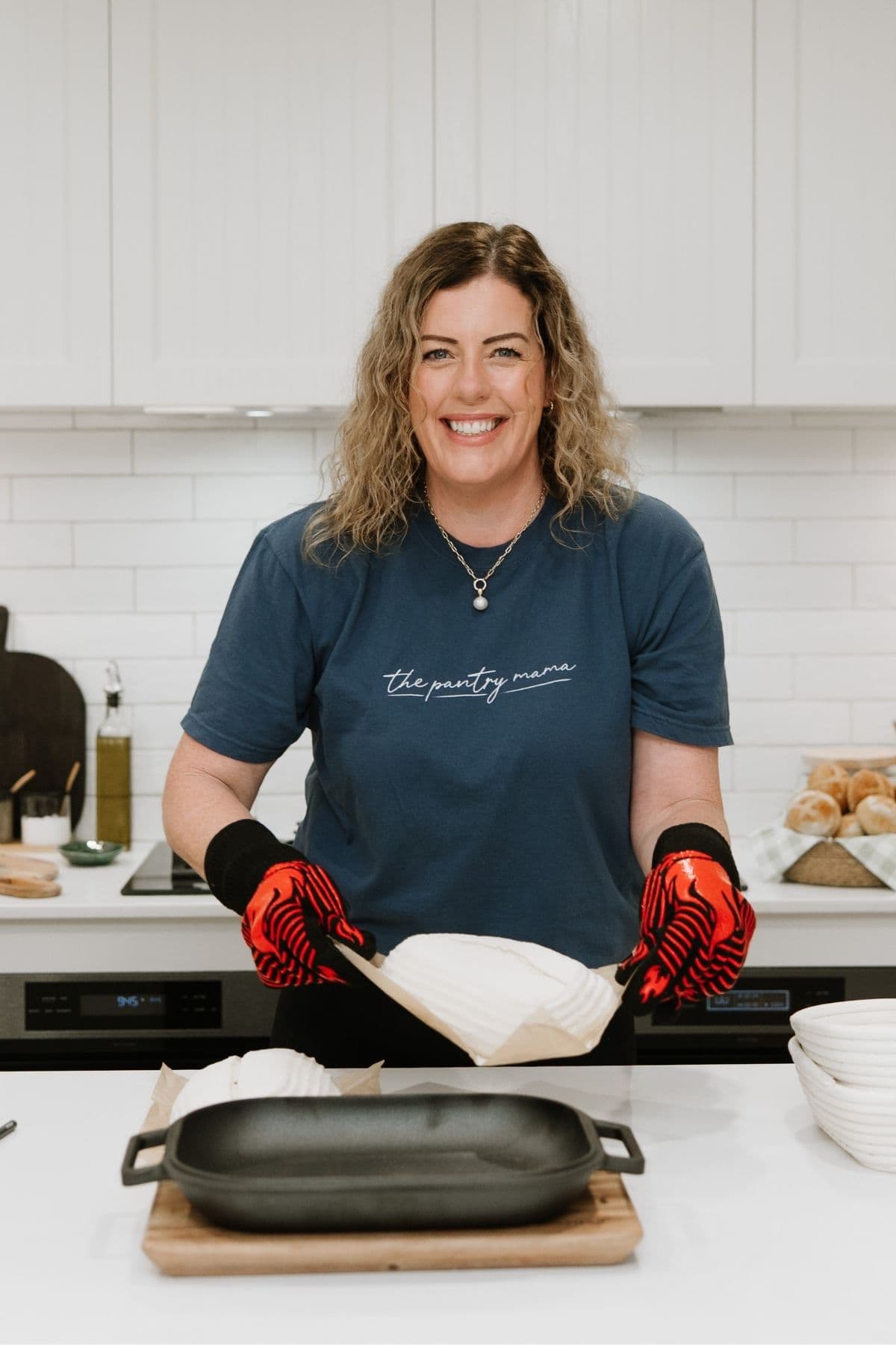 A photo of Kate Freebairn, founder of The Pantry Mama, placing a loaf of sourdough into a black cast-iron bread pan ready to place it into the oven.