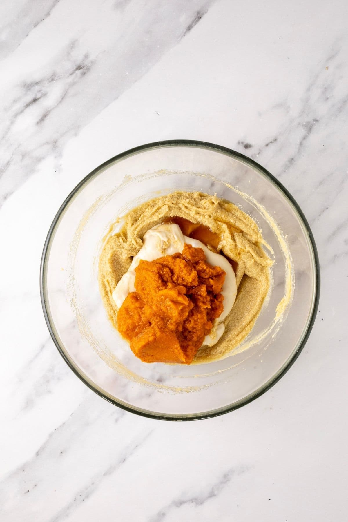 A glass bowl showing sourdough starter, pumpkin puree and vanilla being added to the bowl. 