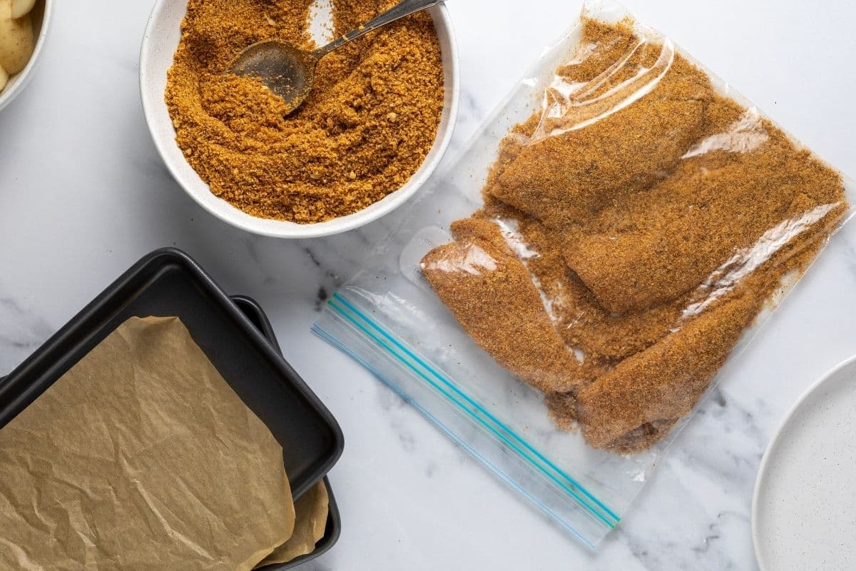 A horizontal image showing a bowl of sourdough shake and bake as well as a resealable plastic bag filled with chicken coated in seasoned breadcrumb mix.