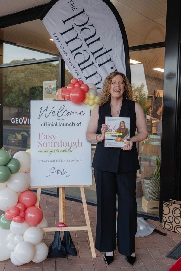 Kate Freebairn from The Pantry Mama standing outside her book launch holding a copy of her book, Easy Sourdough On Any Schedule.